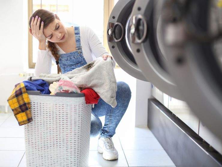 donna disperata con bucato in mano e lavatrice con oblò aperto