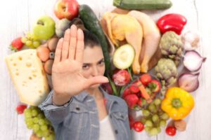 alimenti crudi su sfondo bianco e donna che fa stop con le mani