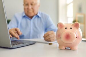 uomo anziana al pc con salvadanaio a forma di maialino